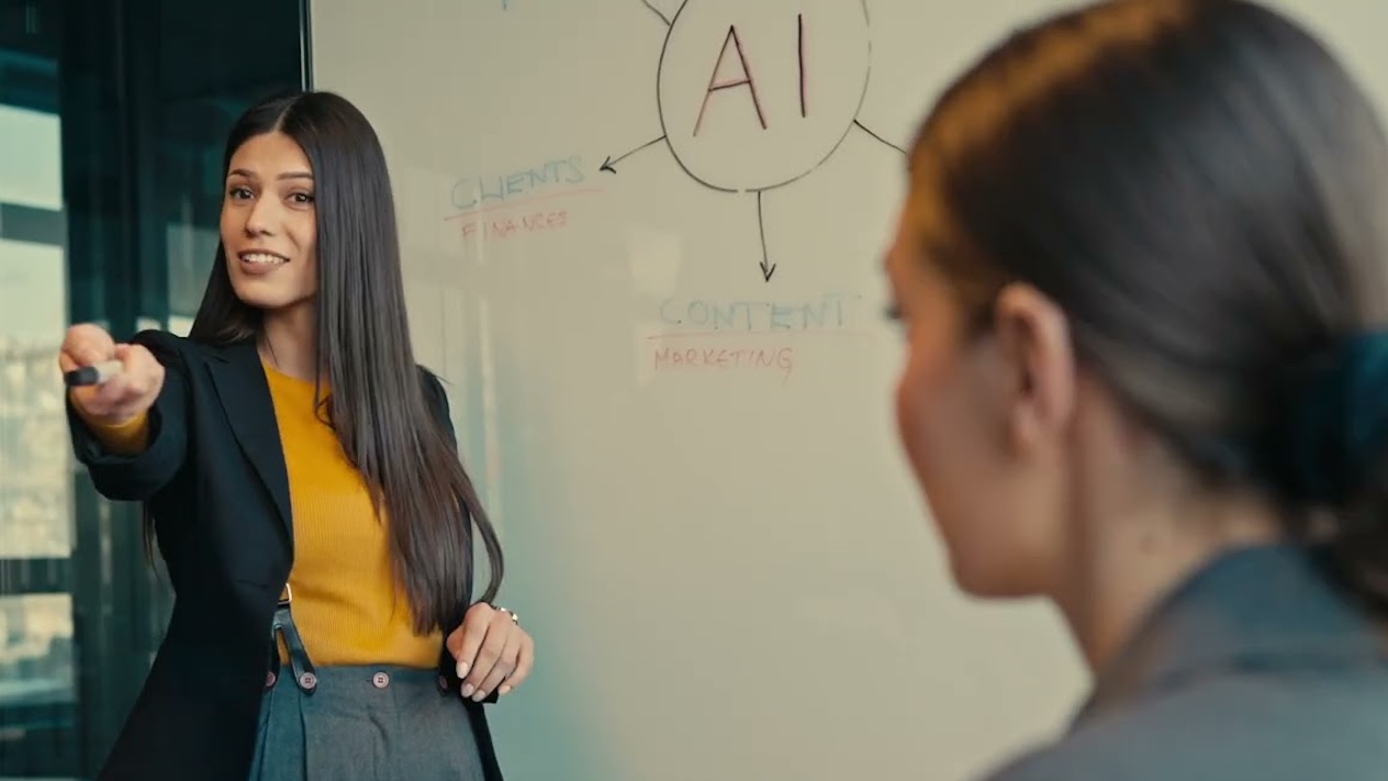 person standing in front of a white board that says "AI", pointing off camera with a marker