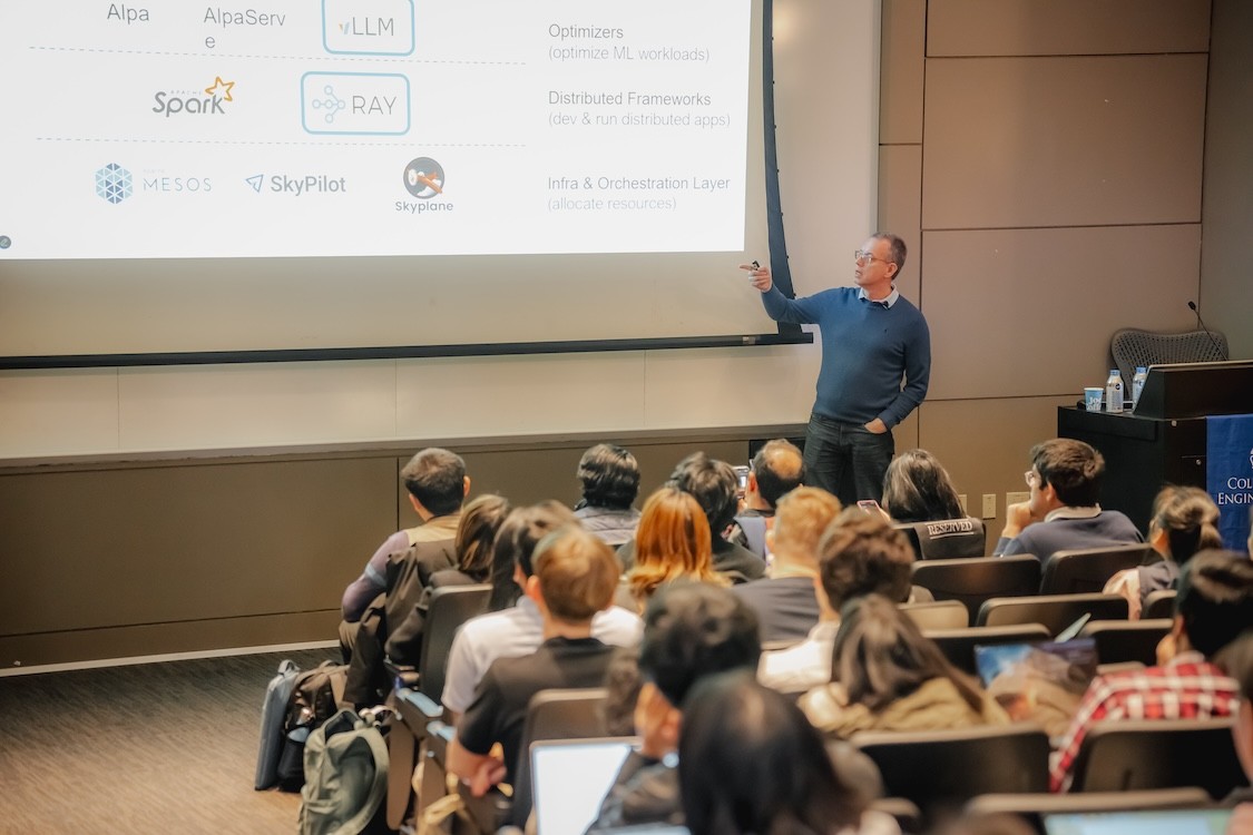 Ion Stoica gesturing towards a screen in a crowded room during his Lecture Series in AI.